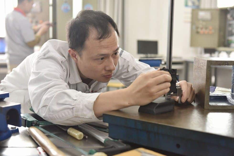A man inspecting a CNC machine part in a manufacturing workshop.
