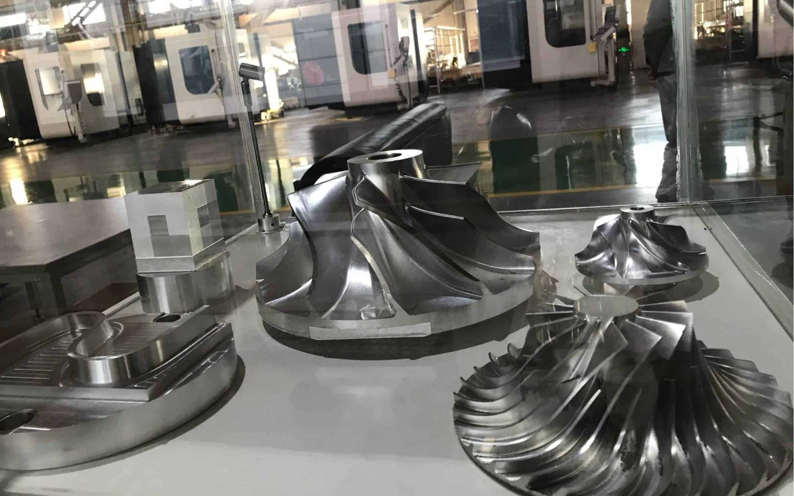 High-precision 5-axis machined metal parts displayed on a glass surface.