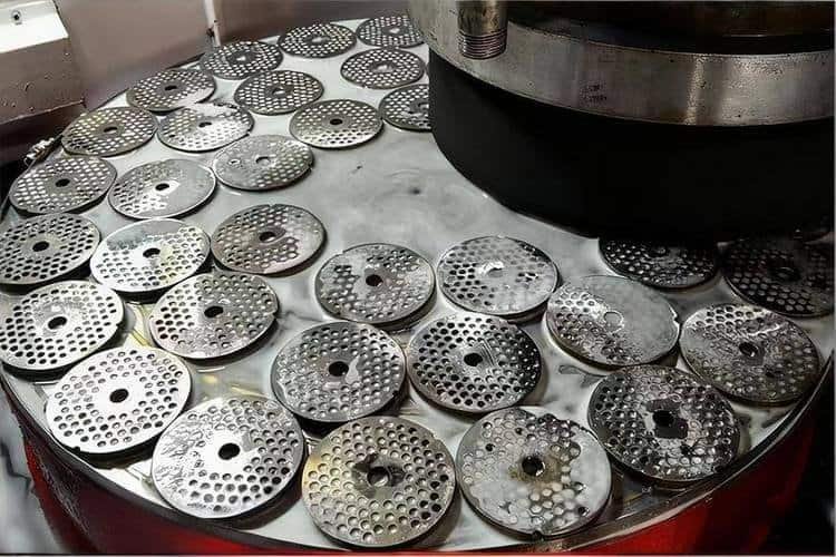 Close-up of CNC machined metal discs with drilled holes on a manufacturing table.