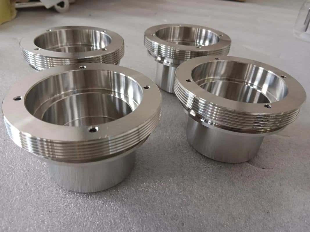 Four machined metal sleeves with external threads and flanges.