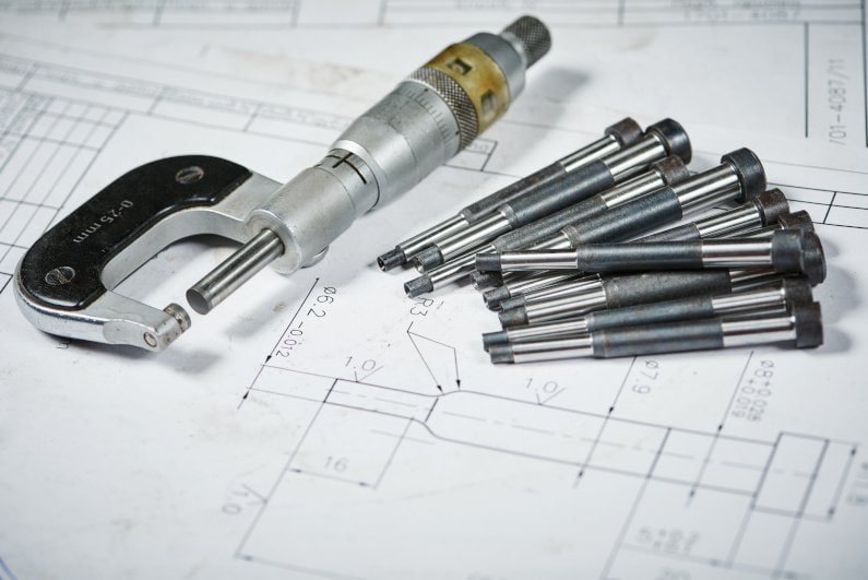Precision measurement tools and CNC machined metal parts on technical drawings.