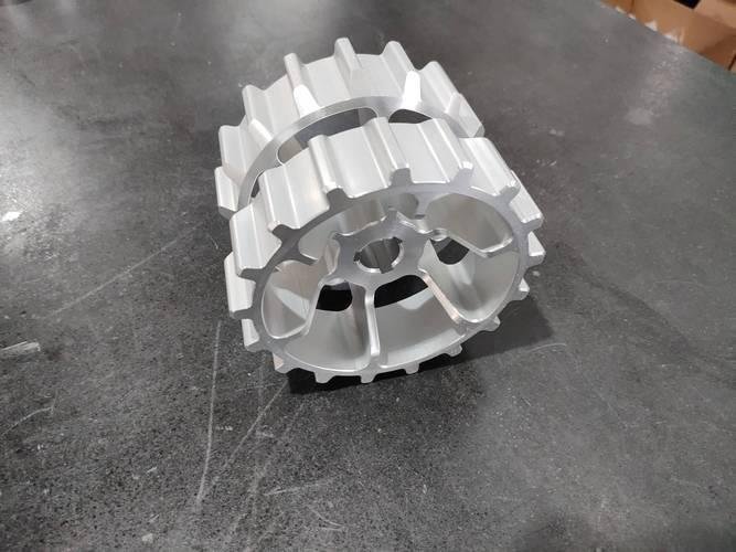 Precision machined aluminum CNC part with gear-like features on a dark surface.