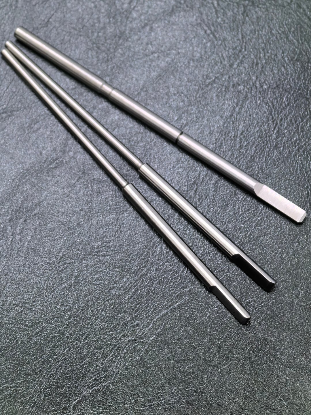 Three slender metal shafts with stepped ends and flats