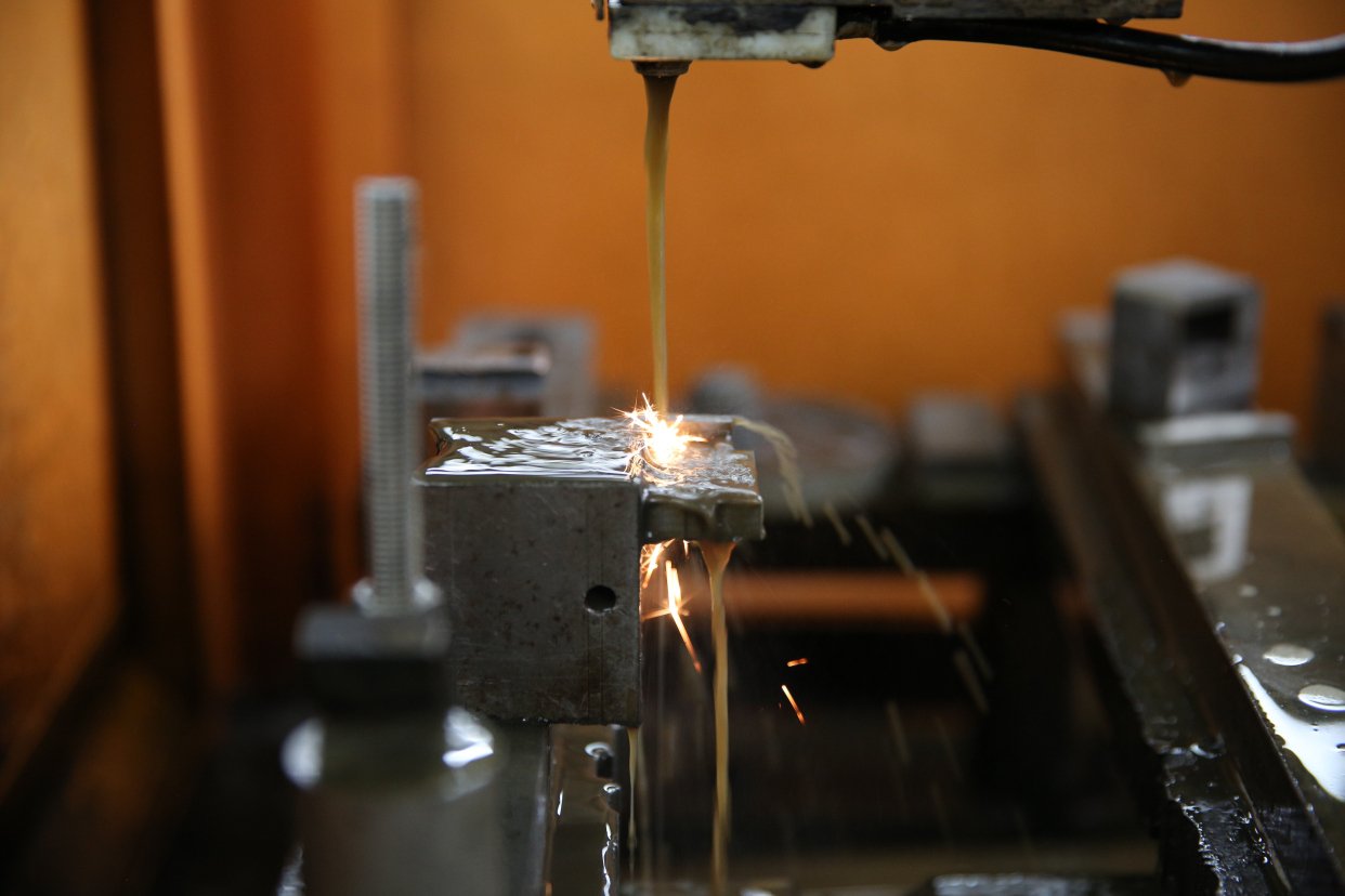 Wire EDM cutting a metal workpiece with visible electrical discharge